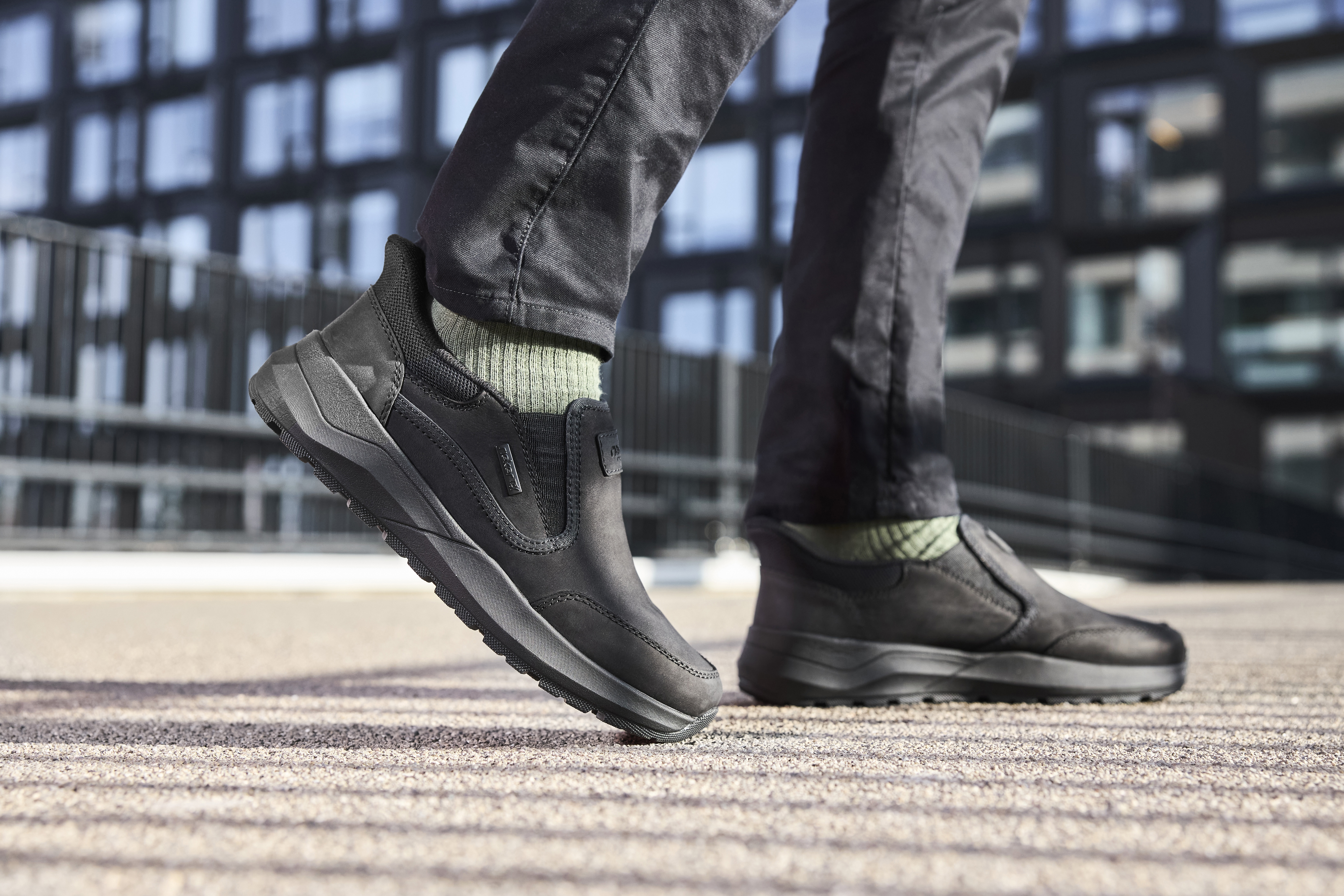 Man presenteert bruine Rieker herensneakers met grijze accenten en stevige lichtgewicht zool, ideaal voor dagelijks gebruik en comfort.