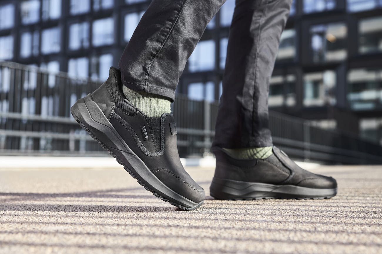 Man presenteert bruine Rieker herensneakers met grijze accenten en stevige lichtgewicht zool, ideaal voor dagelijks gebruik en comfort.