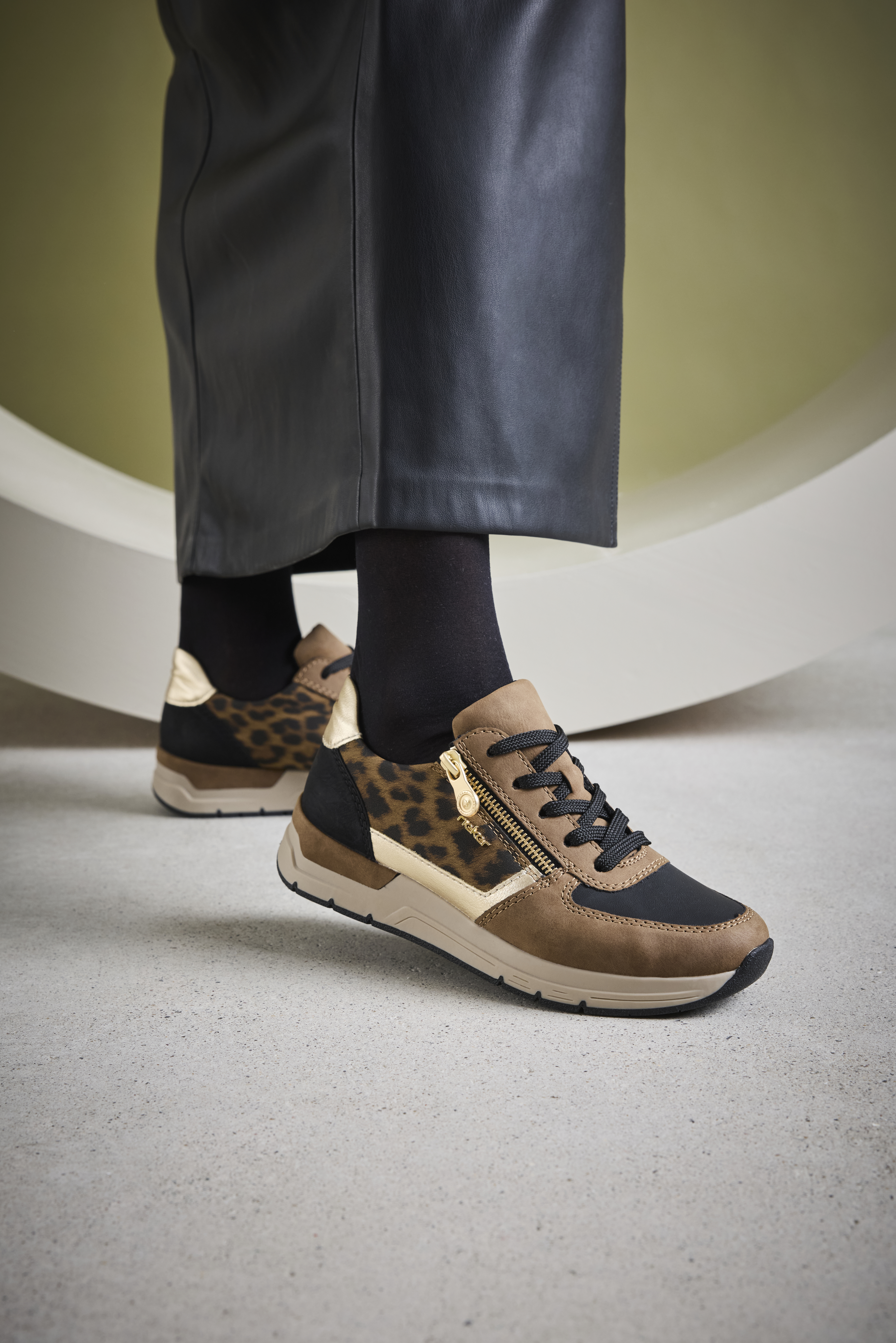 Trendy Rieker damessneakers met luipaardprint en goudkleurige rits, gedragen met zwarte kousen en een leren rok voor een stoere, stijlvolle look.