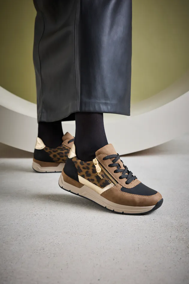 Trendy Rieker damessneakers met luipaardprint en goudkleurige rits, gedragen met zwarte kousen en een leren rok voor een stoere, stijlvolle look.