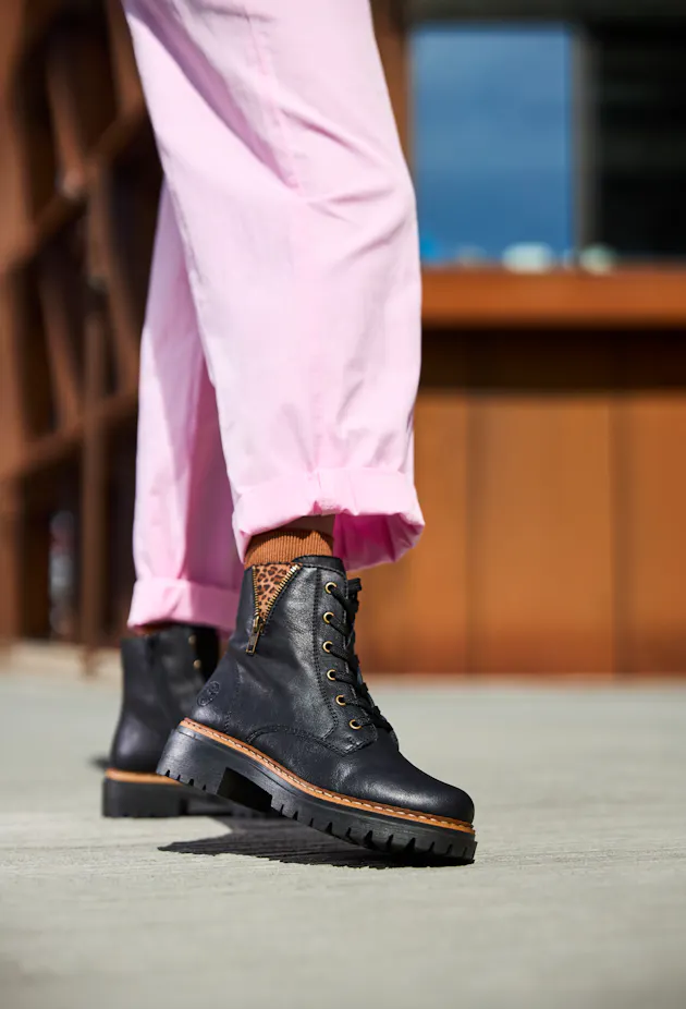 Close-up van zwarte Rieker dames veterboots met rits en stoere profielzool, gedragen met opgerolde roze broek en bruine sokken met luipaarddetail.