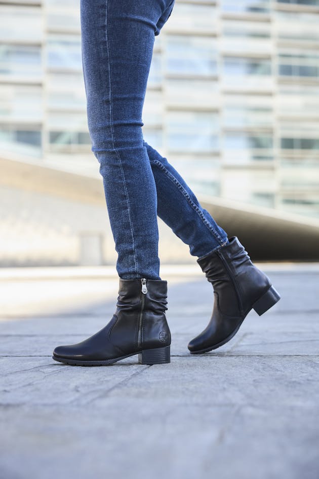 Close-up van zwarte dames enkellaarzen met lage hak en ritssluiting, gedragen met een blauwe skinny jeans op straat, voor een casual en elegante look.