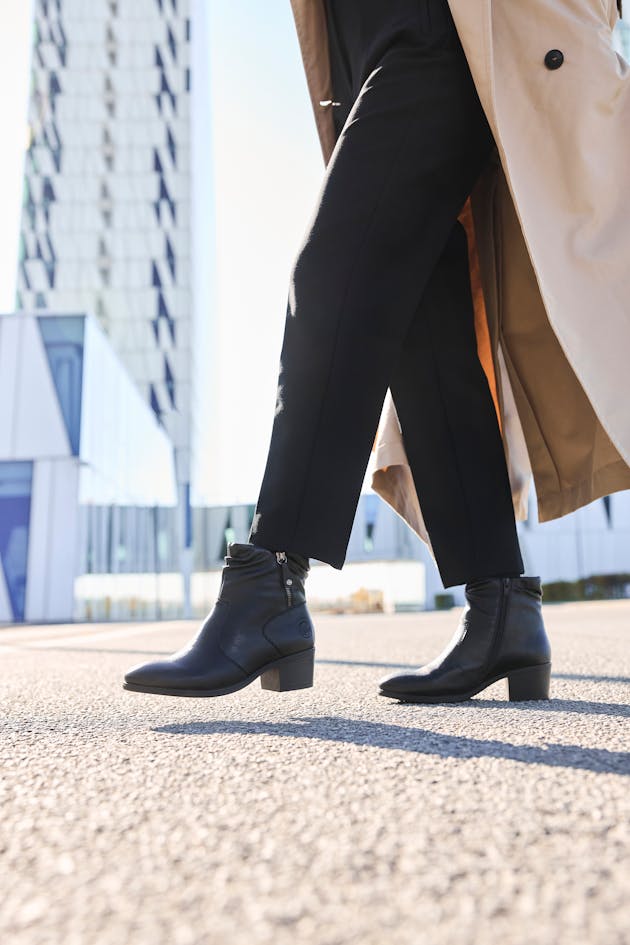 Dame loopt buiten in zwarte Rieker enkellaarsjes met lage hak en rits, perfect voor een elegante maar comfortabele look.