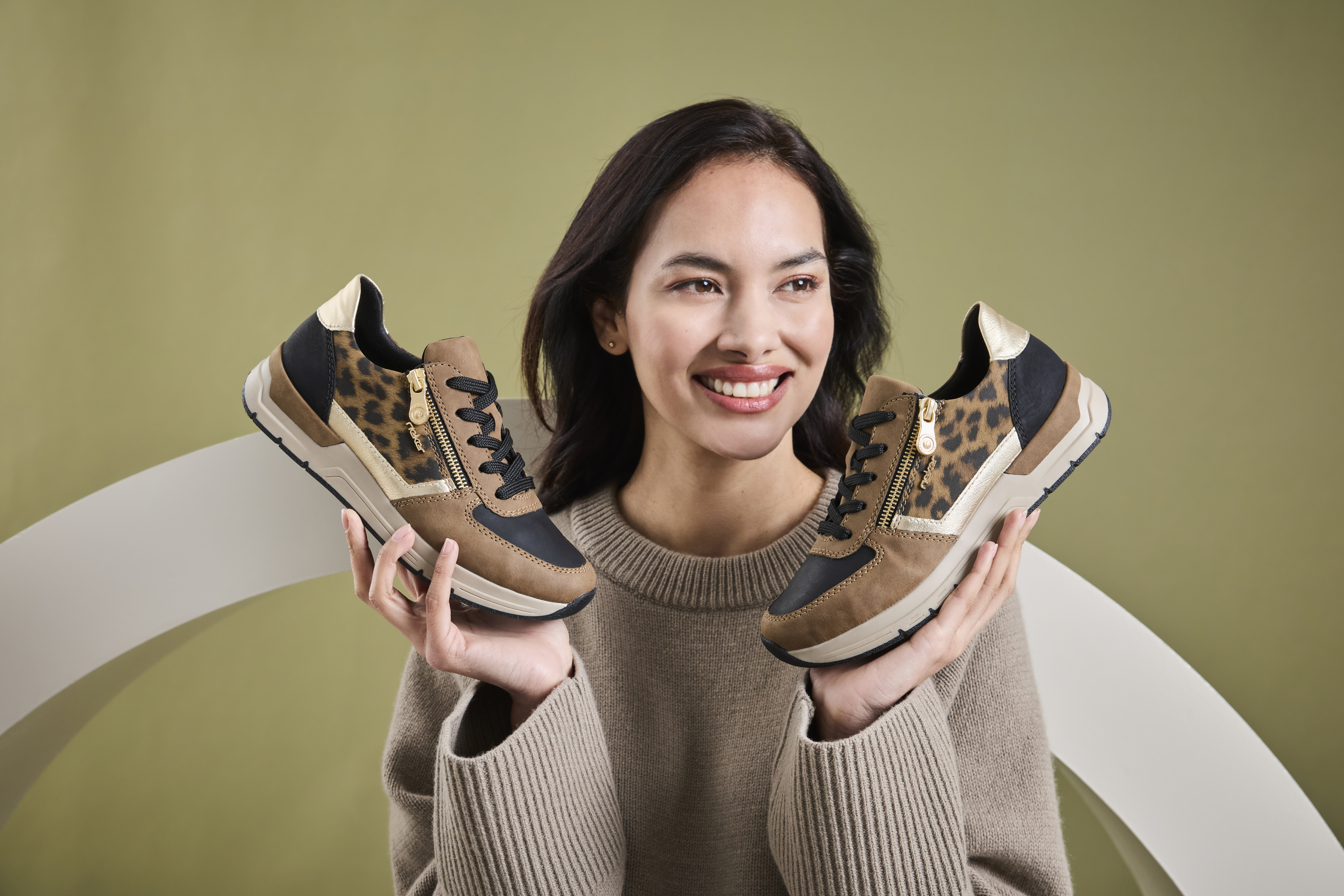 Vrouw houdt een paar Rieker sneakers vast met luipaardprint, beige en zwarte accenten, en lichte zool voor optimaal draagcomfort.