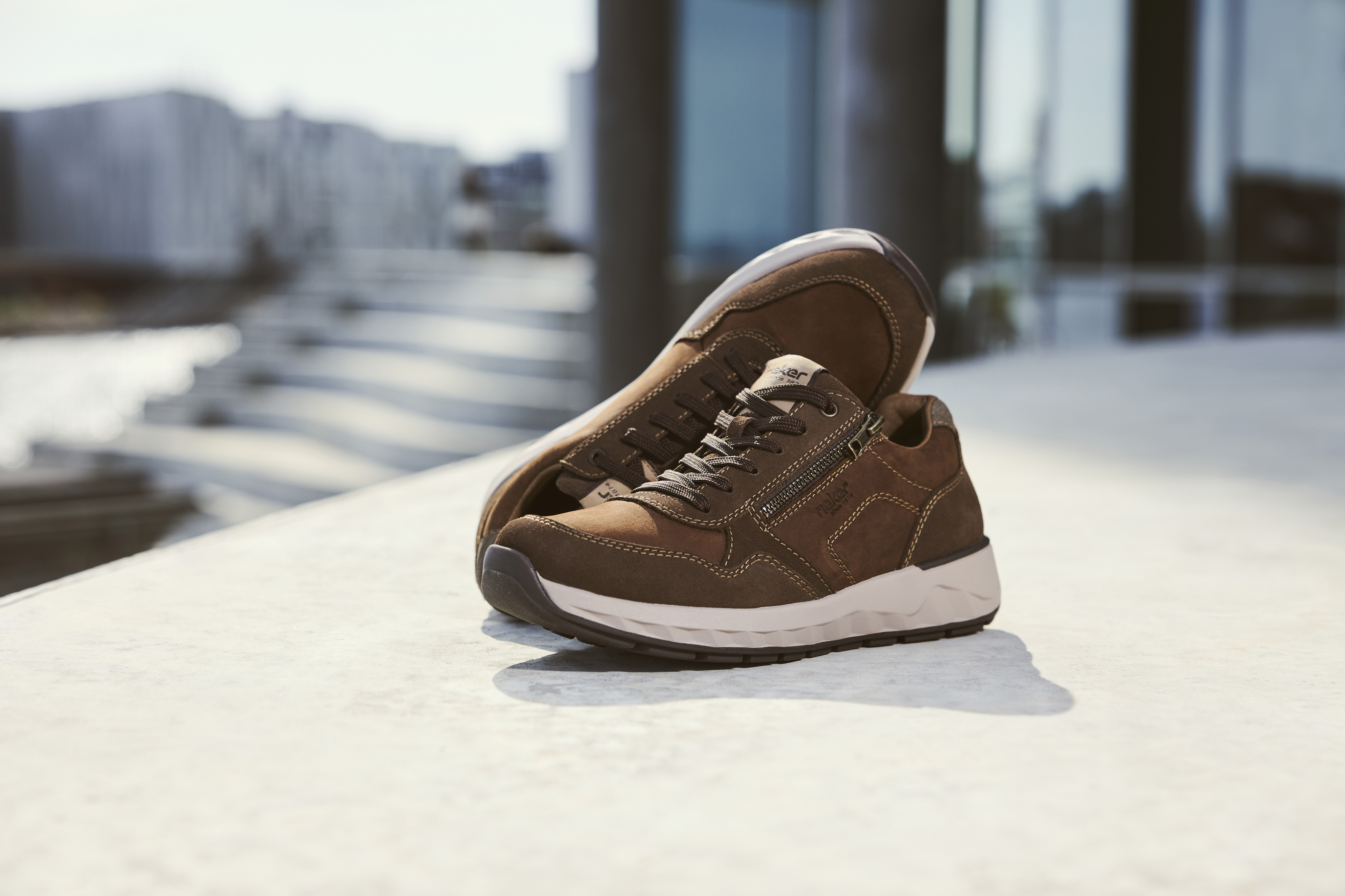 Vrouw houdt een paar Rieker sneakers vast met luipaardprint, beige en zwarte accenten, en lichte zool voor optimaal draagcomfort.