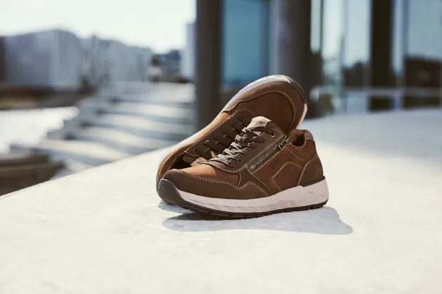 Vrouw houdt een paar Rieker sneakers vast met luipaardprint, beige en zwarte accenten, en lichte zool voor optimaal draagcomfort.