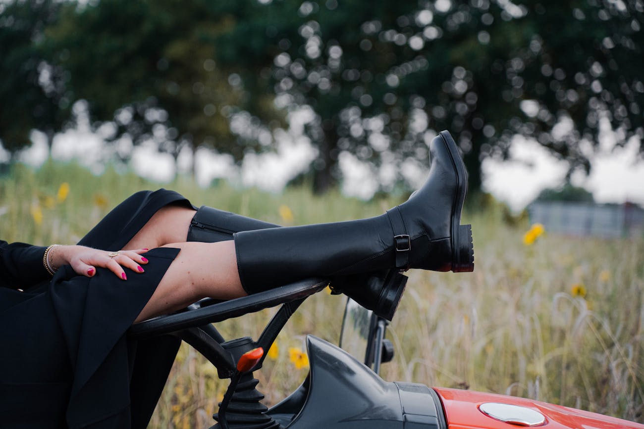 Vrouw toont zwarte leren dameslaarzen met gespdetail, hoog model met stevige zool, gedragen in een veld met zonnebloemen voor een stoere en elegante uitstraling.