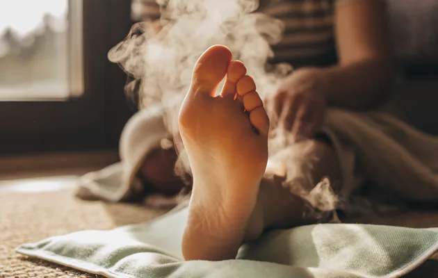 Close-up van een voet die rust op een warmtekussen, met opstijgende stoom en warm zonlicht voor een ontspannen, huiselijke sfeer.