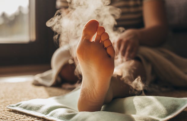 Close-up van een voet die rust op een warmtekussen, met opstijgende stoom en warm zonlicht voor een ontspannen, huiselijke sfeer.