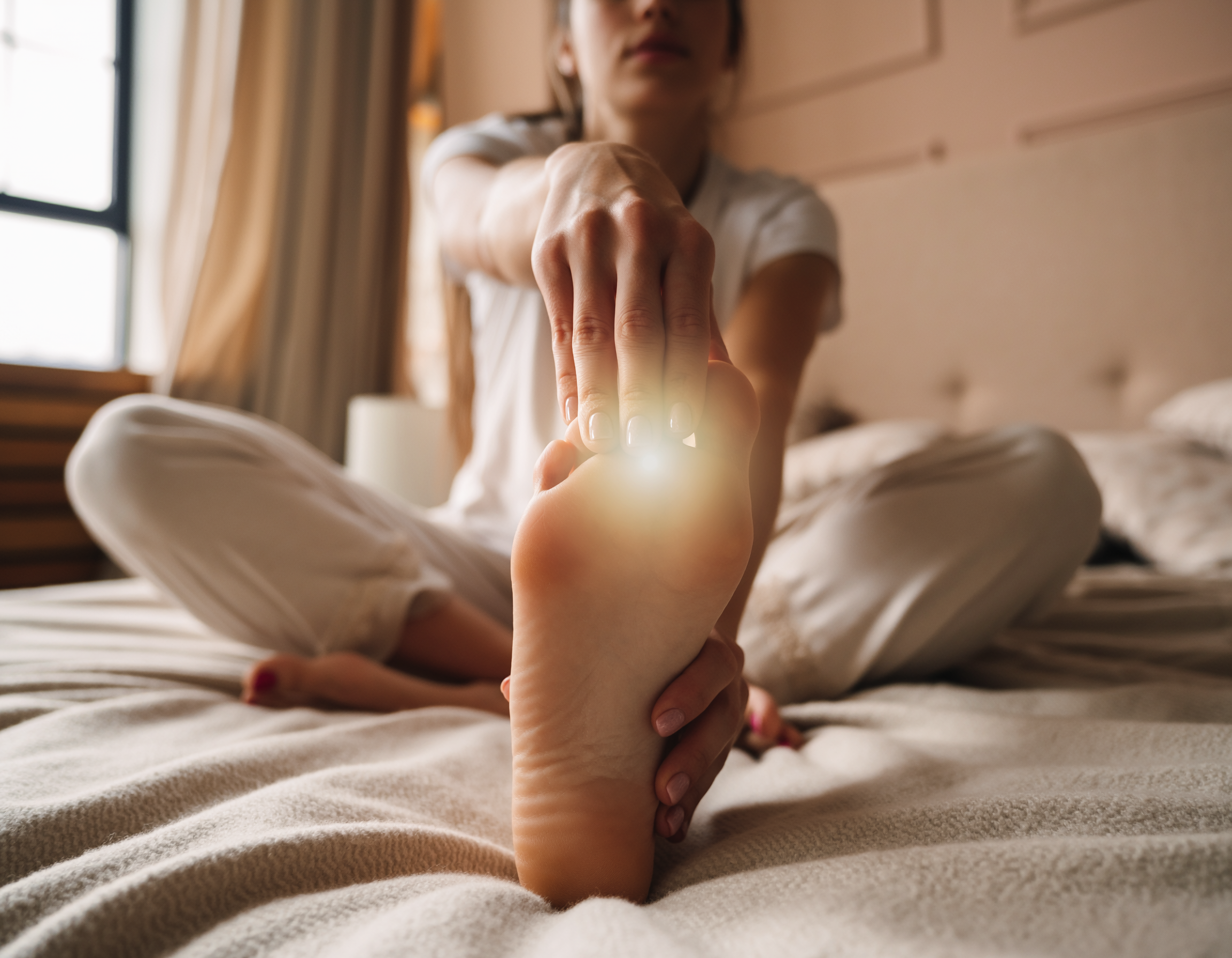 Close-up van een persoon die rustig de voet strekt op bed, met warm ochtendlicht en een zachte, huiselijke sfeer.