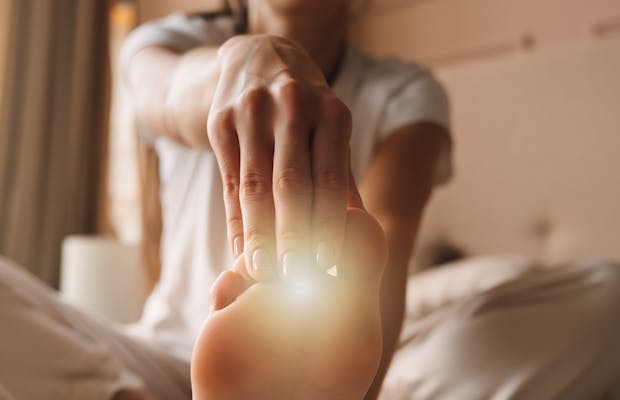Close-up van een persoon die rustig de voet strekt op bed, met warm ochtendlicht en een zachte, huiselijke sfeer.